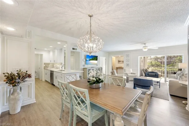 Dining area with a textured ceiling, light wood-type flooring, a decorative wall, a ceiling fan, and a chandelier