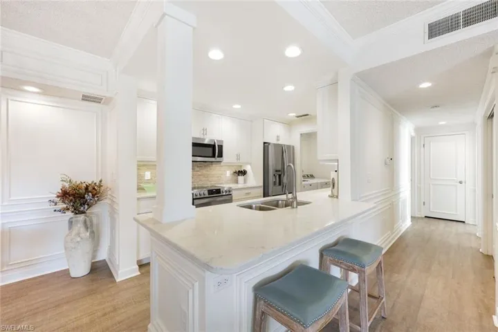 Kitchen with white cabinets, light wood finished floors, stainless steel appliances, light stone countertops, and a peninsula