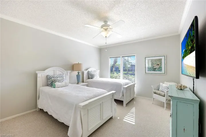 Bedroom featuring a textured ceiling, light colored carpet, ceiling fan, and crown molding