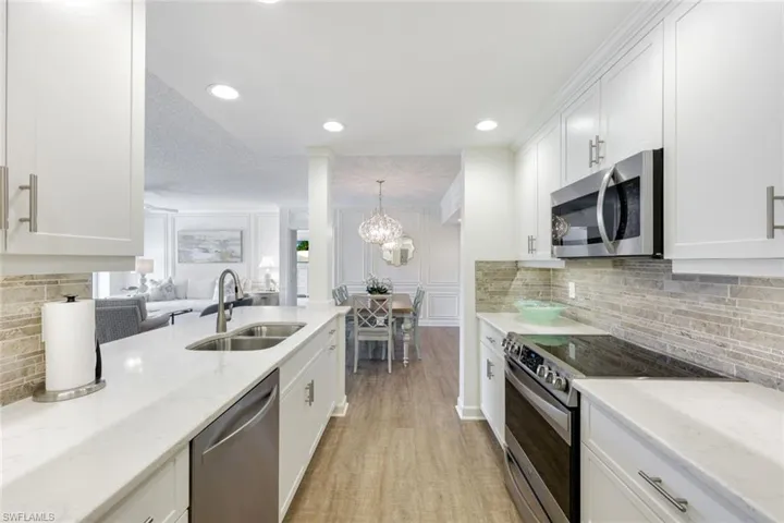 Kitchen with backsplash, stainless steel appliances, white cabinets, and light stone countertops