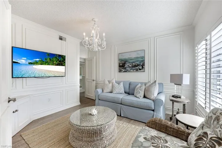 Living room featuring a decorative wall, light wood-style floors, a textured ceiling, suspended lighting, and ornamental molding