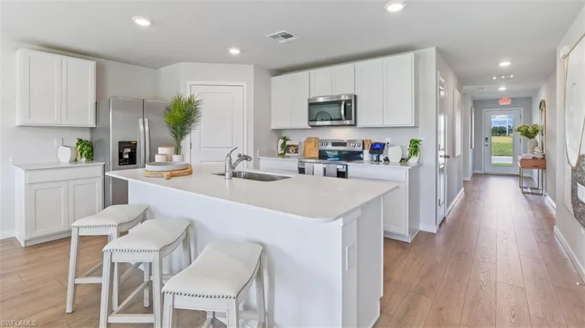 Model home. Kitchen featuring stainless steel appliances, white cabinetry, a breakfast bar, light wood-type flooring, and recessed lighting