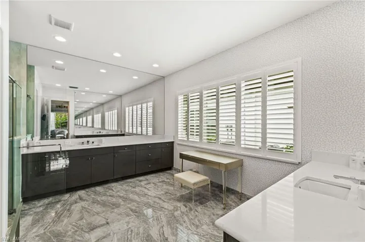 Primary suite bathroom with sleek cabinetry, plantation shutters, dual vanities, walk-in shower, water closet.
