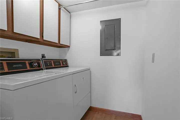 Laundry area featuring wood finished floors, baseboards, washer and dryer, cabinet space, and electric panel