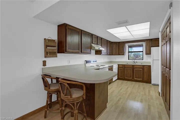 Kitchen featuring light wood-style floors, a sink, a peninsula, white appliances, and under cabinet range hood