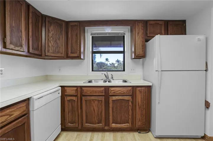 Kitchen featuring light countertops, white appliances, a sink, and light wood-style floors
