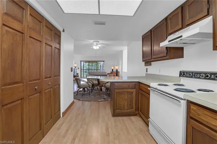 Kitchen featuring light wood finished floors, electric stove, a peninsula, light countertops, and under cabinet range hood