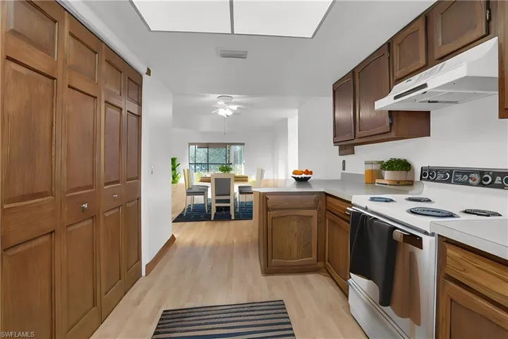 Virtually Staged Kitchen with light wood-type flooring, light countertops, under cabinet range hood, and white electric range oven