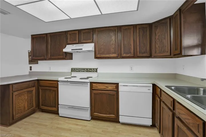 Kitchen with under cabinet range hood, white appliances, a sink, light wood-style floors, and light countertops