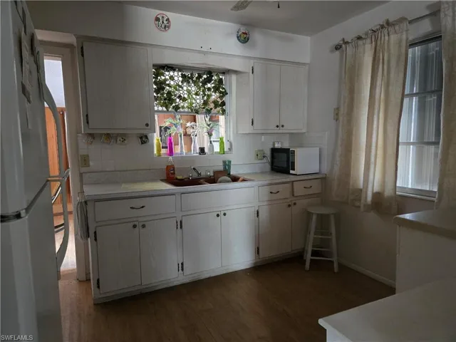 Kitchen featuring tasteful backsplash, dark wood-type flooring, a sink, black microwave, and freestanding refrigerator