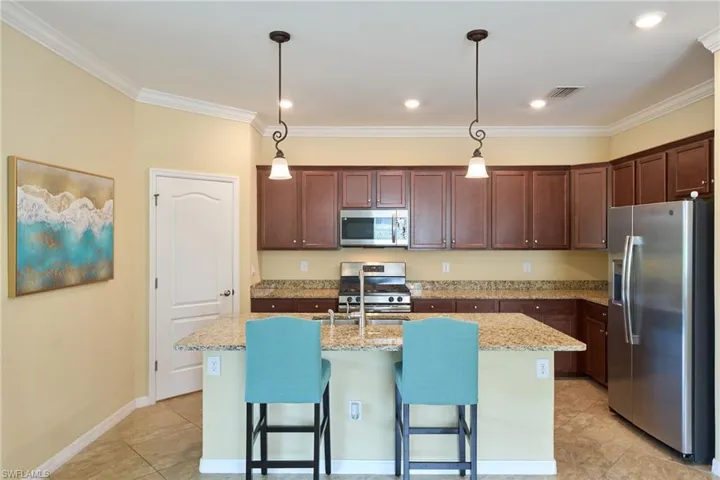 Kitchen featuring appliances with stainless steel finishes, decorative light fixtures, light tile patterned floors, and a center island with sink