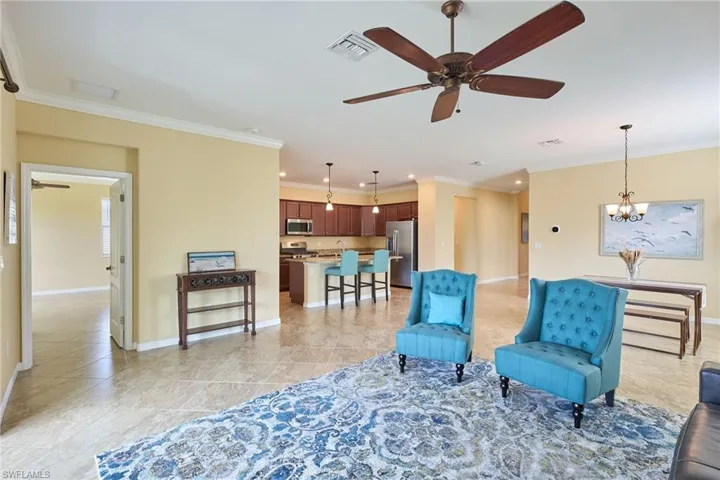 Living area featuring ceiling fan with notable chandelier, light tile patterned floors, and crown molding