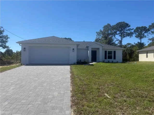 Ranch-style home featuring a front lawn, an attached garage, decorative driveway, and stucco siding