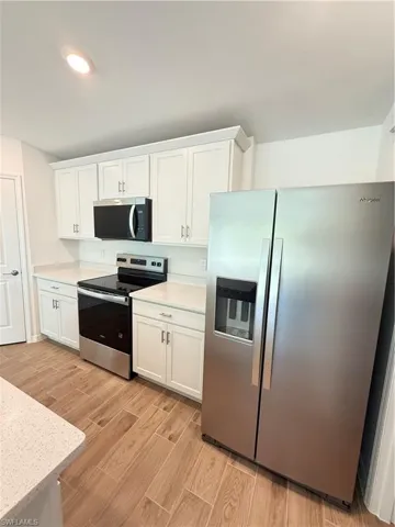 Kitchen featuring stainless steel appliances, white cabinetry, wood finish floors, light stone countertops, and recessed lighting