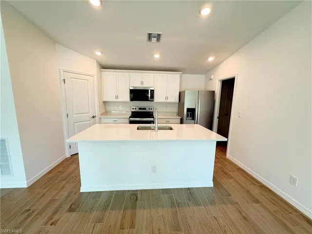 Kitchen featuring white cabinetry, stainless steel appliances, wood tiled floors, a center island with sink, and light stone counters