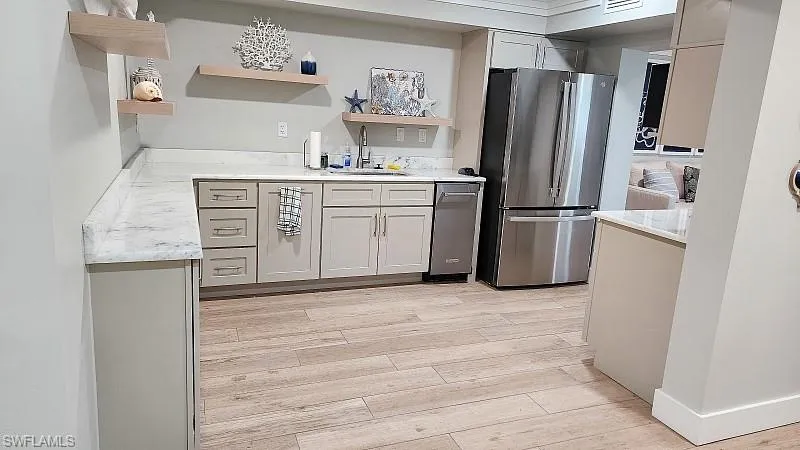 Community RM Kitchen featuring open shelves, stainless steel appliances, light wood-style floors, and light stone countertops