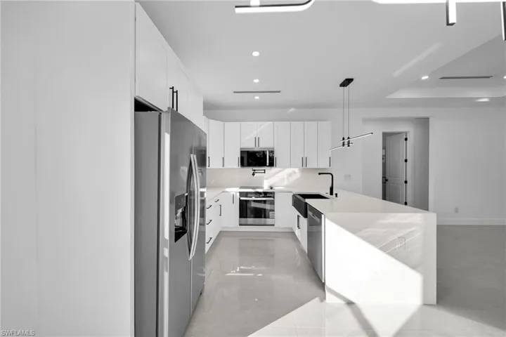 Kitchen with appliances with stainless steel finishes, white cabinets, light stone countertops, recessed lighting, and a peninsula