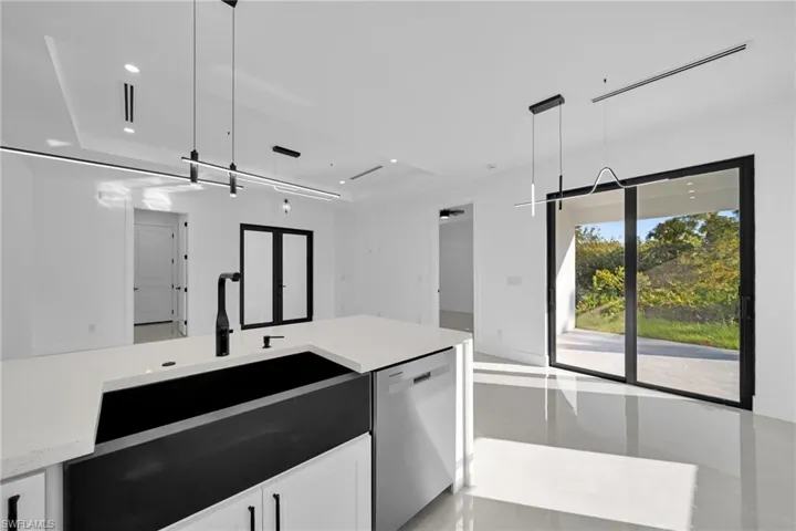 Kitchen with stainless steel dishwasher, light stone counters, decorative light fixtures, white cabinetry, and open floor plan