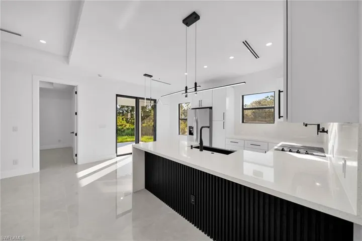 Kitchen with light stone counters, decorative light fixtures, plenty of natural light, recessed lighting, and white cabinets
