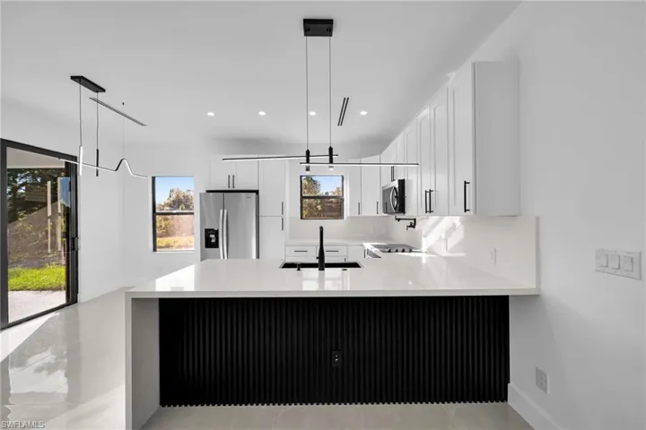 Kitchen with pendant lighting, light stone counters, a peninsula, stainless steel appliances, and white cabinets