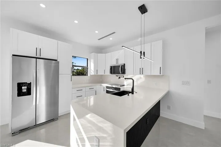 Kitchen with appliances with stainless steel finishes, a peninsula, white cabinets, light stone countertops, and recessed lighting