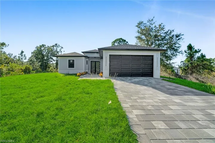 Prairie-style home featuring a front yard, decorative driveway, stucco siding, and an attached garage