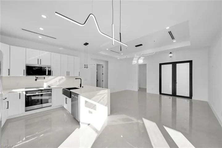 Kitchen with a raised ceiling, white cabinetry, a peninsula, open floor plan, and appliances with stainless steel finishes