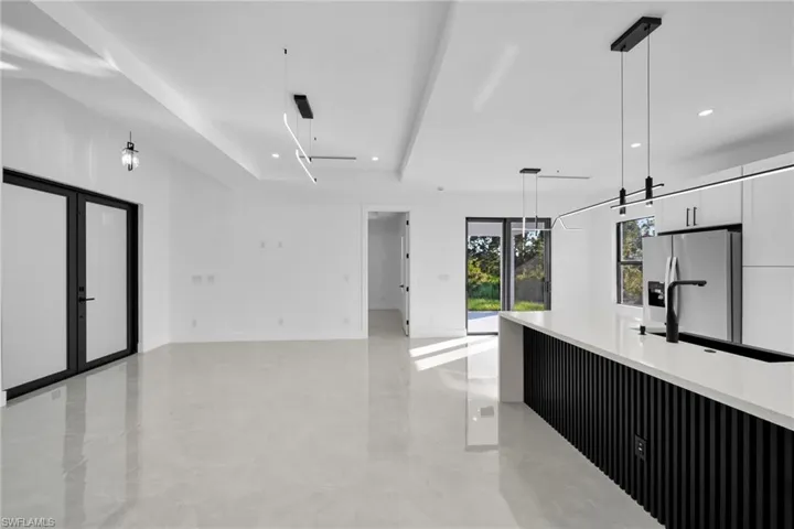 Kitchen with hanging light fixtures, modern cabinets, white cabinets, a raised ceiling, and light stone counters