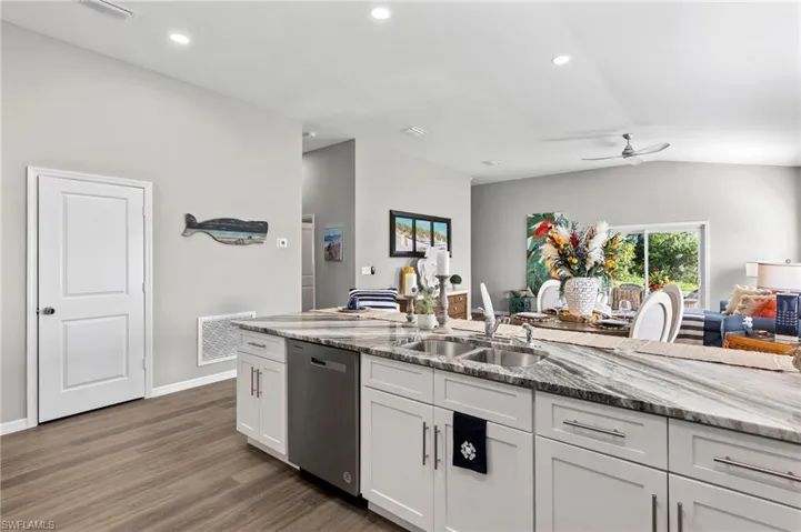 Kitchen featuring open floor plan, ceiling fan, stainless steel dishwasher, light stone counters, and white cabinetry