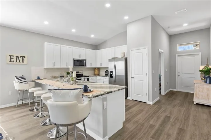 Kitchen featuring white cabinets, a kitchen breakfast bar, light stone counters, a peninsula, and light wood finished floors