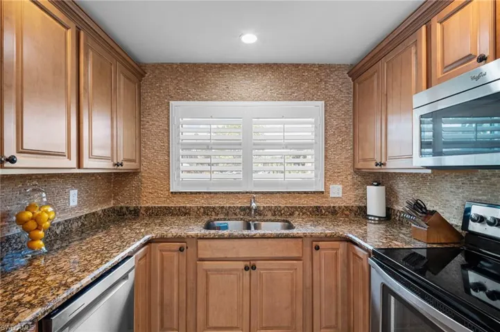 Kitchen featuring appliances with stainless steel finishes, backsplash, brown cabinets, dark stone counters, and recessed lighting