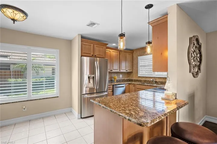 Kitchen with a peninsula, appliances with stainless steel finishes, a breakfast bar area, dark stone countertops, and light tile patterned floors