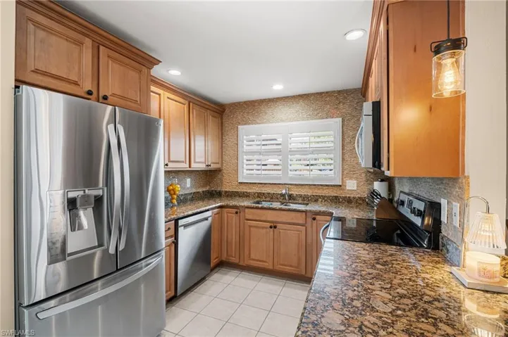 Kitchen featuring appliances with stainless steel finishes, tasteful backsplash, light tile patterned flooring, brown cabinetry, and recessed lighting