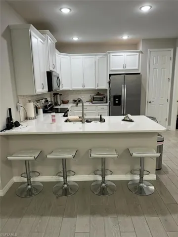 Kitchen with kitchen peninsula, appliances with stainless steel finishes, a kitchen bar, white cabinets, and light wood-type flooring