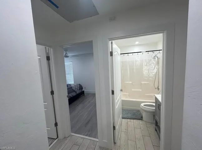 Full bathroom with vanity, shower / tub combo with curtain, light wood finished floors, ensuite bathroom, and a textured wall
