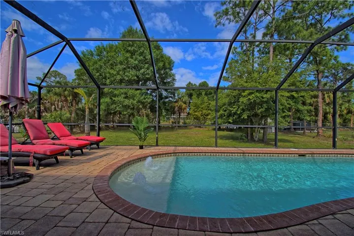 The property features a screened-in swimming pool area with a paver patio, offering clear views of the surrounding green landscape and mature trees
