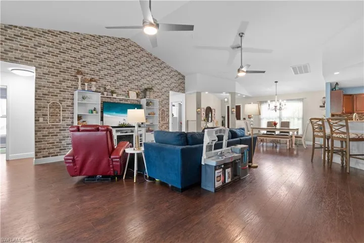 Expansive open concept living area featuring dark wood flooring, a vaulted ceiling, and a brick accent wall