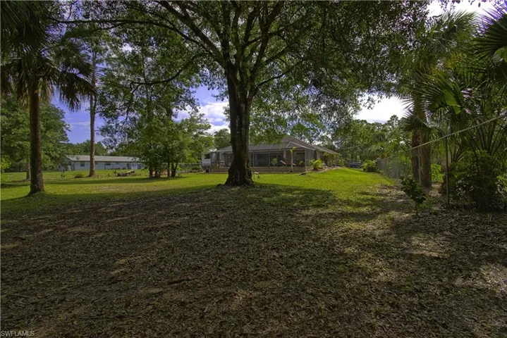 The property features a spacious yard with a lush lawn and a variety of mature trees, including palm trees