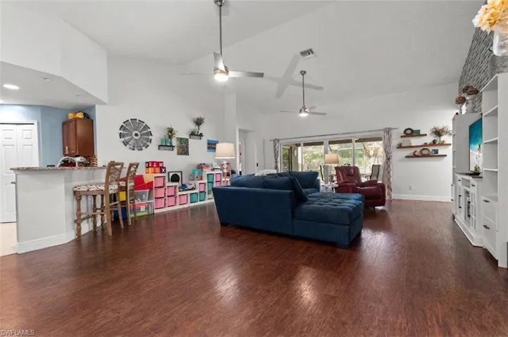 Open concept living space featuring rich wood flooring, vaulted ceilings with ceiling fans, and large sliding glass doors providing outdoor access
