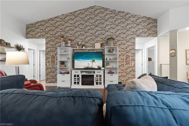 Living room featuring vaulted ceilings, a prominent brick accent wall, and wood flooring