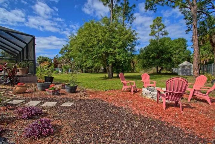 The property features a spacious yard with a screened enclosure, a fire pit area surrounded by four Adirondack chairs, and a garden shed