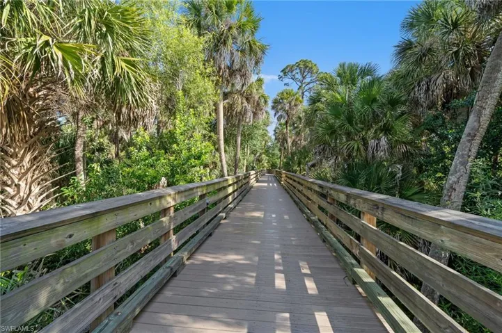The community features a wooden boardwalk surrounded by palm trees and lush greenery