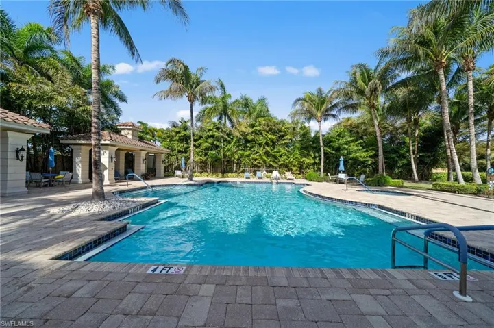 The community features a large outdoor swimming pool with a paved patio surround, set amongst mature palm trees and lush landscaping