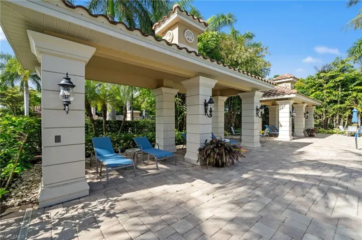 Shaded patio area featuring a tiled roof structure, decorative wall sconces, and paver flooring