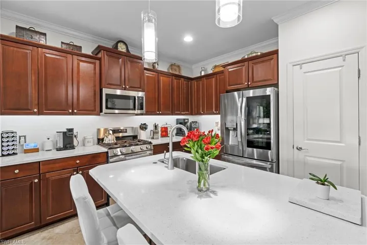 The kitchen features extensive wood cabinetry, stainless steel appliances, and a central island with a sink and a light-colored countertop