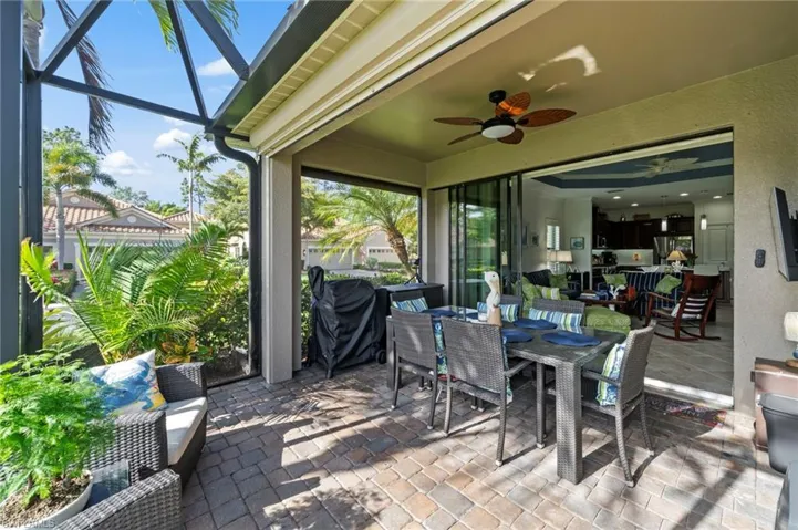 Expansive screened-in lanai with paver flooring, an outdoor ceiling fan, and sliding glass doors providing outdoor living space