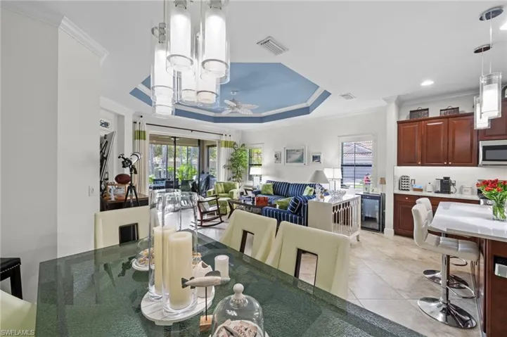 This open-concept living area features a bright blue tray ceiling with a fan, recessed lighting, and crown molding