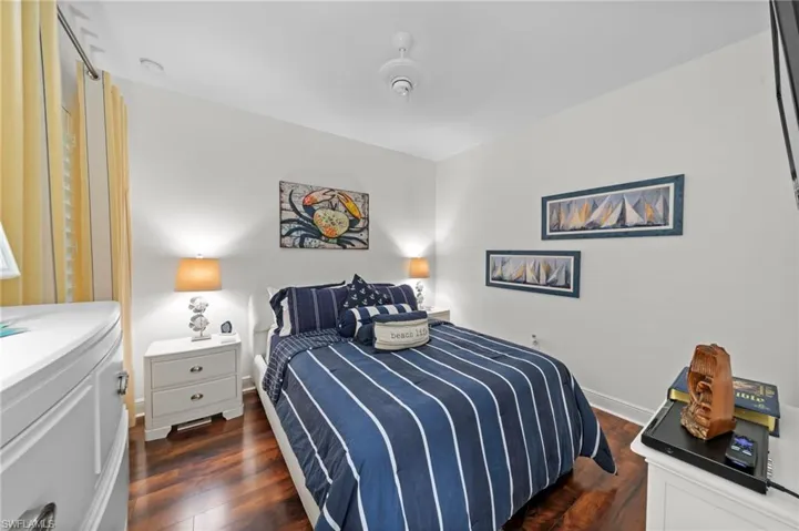 This sleeping area features rich wood flooring, crisp white walls, and a ceiling fan