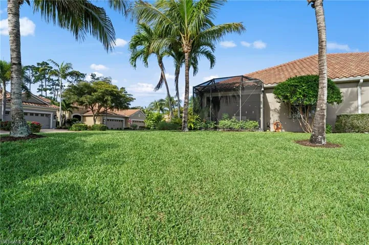The property features a well-maintained lawn, mature palm trees, and an enclosed screened patio area