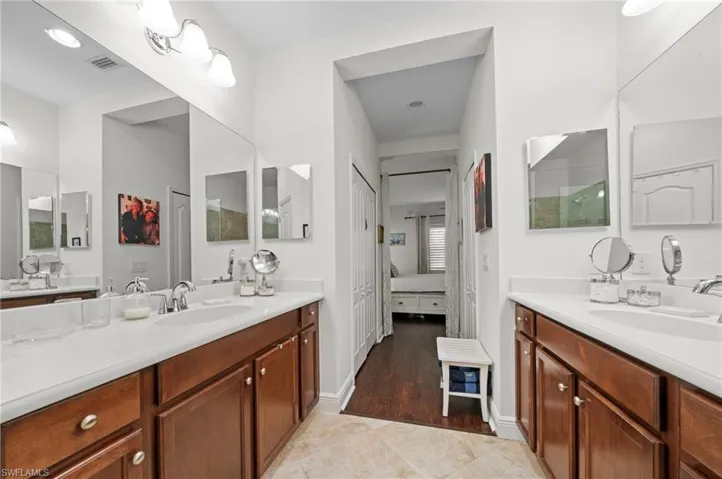 This bathroom features two vanities with white countertops and wooden cabinetry, each with a sink and mirror